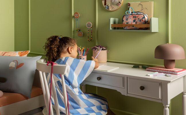 espaço de estudo infantil com escrivaninha, cadeira, luminária de mesa, entre outros itens