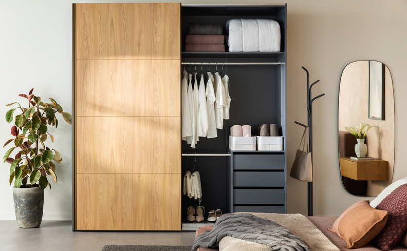 guarda-roupa black friday com portas de correr em um quarto com vaso com planta, espelho grande, cama posta com diversas almofadas.