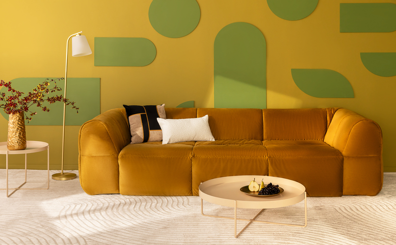 sofá na black friday em um tom de mostarda na sala de estar com mesa de centro, tapete, luminária de chão, mesa de apoio com vaso e flores, além de diversas almofadas decorativas.