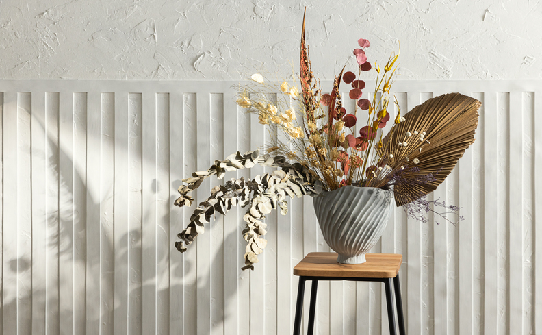 flores para varanda com uma decoração clean e minimalista com tons neutros como branco e madeira clara. Além de um arranjo de flores em um vaso grande em uma mesa de apoio.