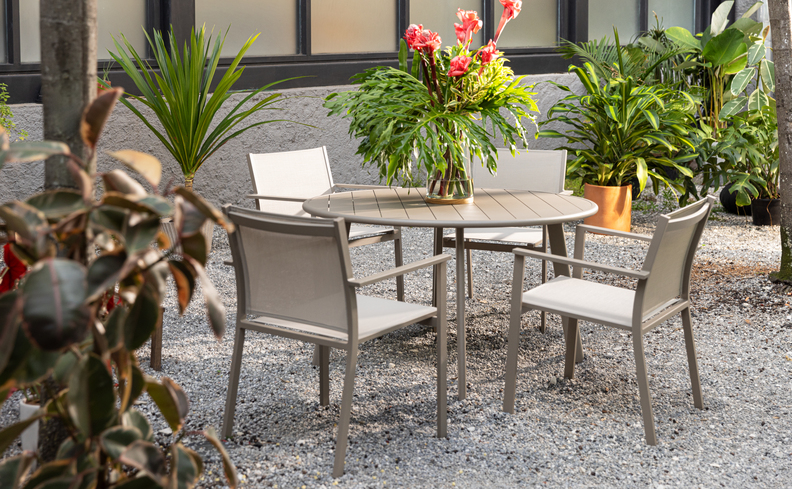 mesa para varanda com quatro cadeiras, mesa redonda de aço, diversas plantas com vasos para deixar o espaço com um toque de natureza.