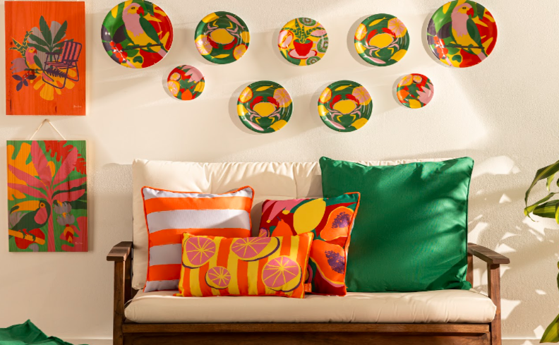 sofá para varanda pequena, com diversas almofadas coloridas, quadros decorativos e pratos na parede para deixar a decoração mais divertida e dinâmica.