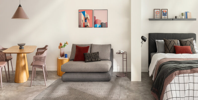 móveis multiuso em um apartamento pequeno com sofá cama, cama, mesa de jantar com quatro cadeiras, estantes nas paredes, quadros e outros itens de decoração.