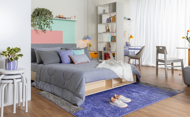 cama baú casal em um quarto integrado com a sala, com cama de casal com nichos, bancos empilháveis, prateleiras, cadeiras, mesas e diversos itens de decoração.