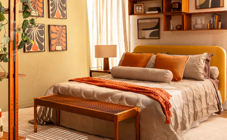 móveis multifuncionais para apartamento com cama de casal, banco, roupa de cama em tons de bege e laranja, quadros de parede, prateleiras e nichos e estante escrivaninha.