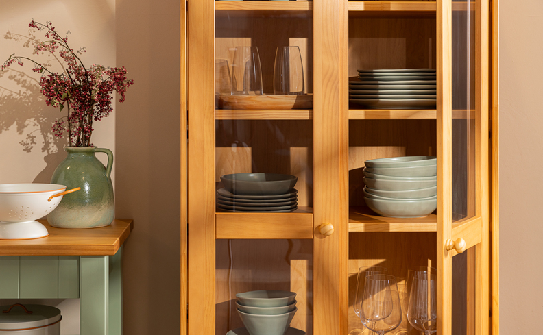 cozinha com cristaleira de madeira e portas de vidro com as louças organizadas e separadas por categorias, além de vasos decorativos com plantas nos tons de verde e branco.