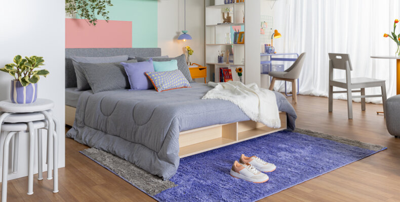 quarto pequeno com cama, tapete, estante dividindo o ambiente, entre outros móveis