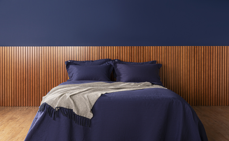 cama casal ou queen em um quarto de tamanho médio com roupa de cama azul e cabeceira em tom de madeira escuro