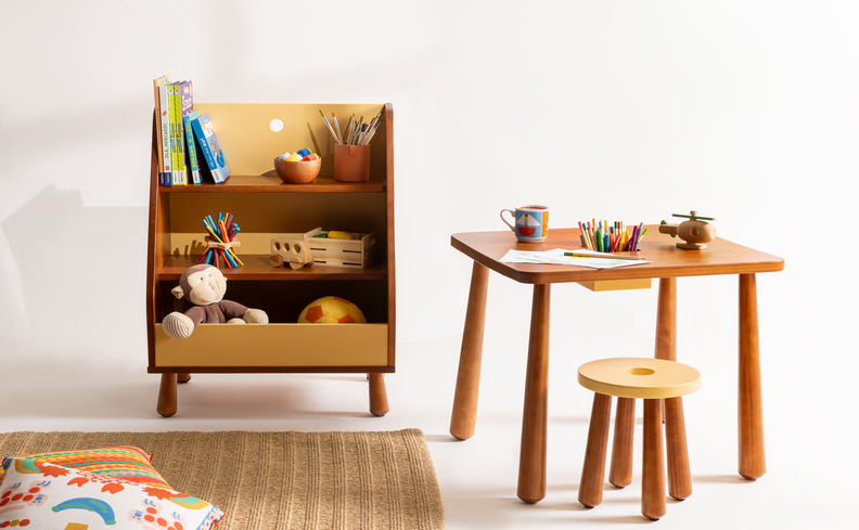 organizadores para quarto infantil com móvel com prateleiras com diversos brinquedos e livros, além de tapete, mesa e cadeira de madeira infantil e almofadas.