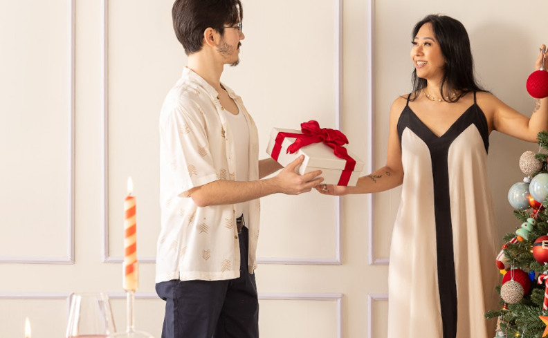 ideias de presente de Natal para toda a família, dois jovens entregando o presente para o outro em uma festa de Natal com toda a família.