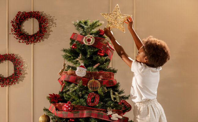criança colocando a estrela na ponta da árvore de natal para completar a decoração de Natal