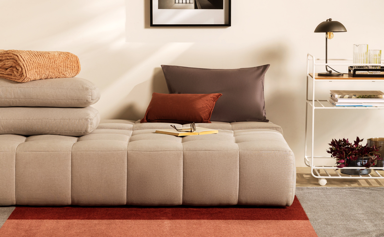 sofá cama para sala pequena com almofadas, carrinho bar com itens de decoração, tapete e quadro decorativo