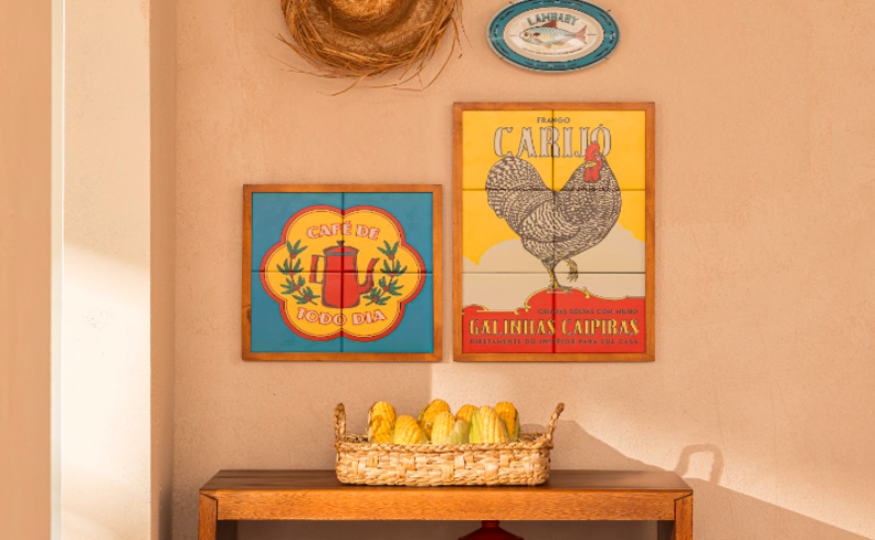 decoração mesa festa junina com aparador de madeira, quadros com diversos desenhos e chapéu de palha na parede para complementar a decoração.