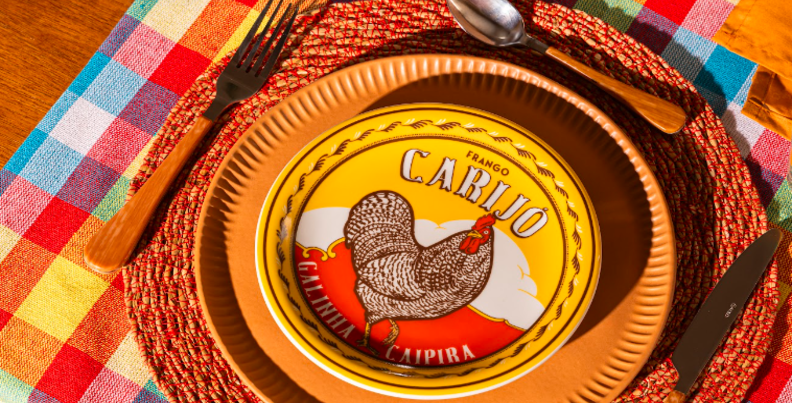 mesa posta festa junina em casa com pratos rasos e fundos com estampa de galinha, jogo americano xadrez, talheres e copos.