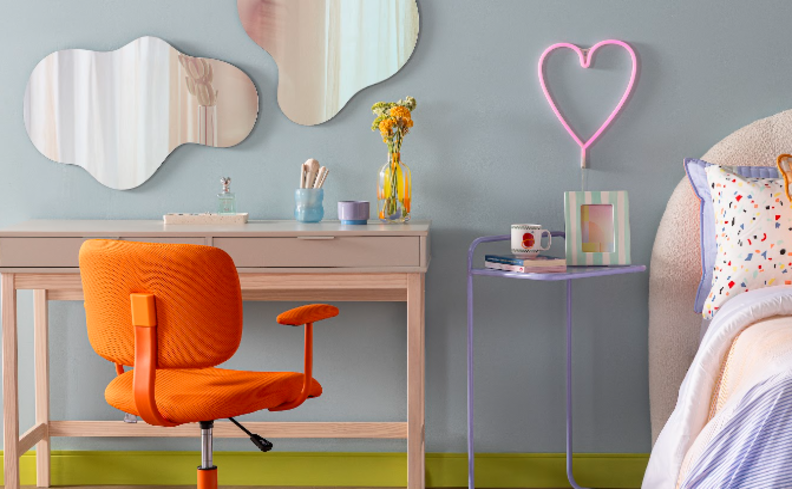 ambiente integrado com home office e quarto com escrivaninha e penteadeira, cama, cadeira laranja para escritório, espelhos nas paredes e diversos itens decorativos.