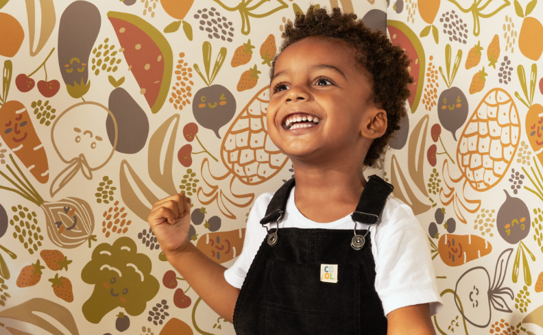 decoração de quarto infantil contendo: menino de pele negra sorrindo, com cabelo cacheado, camiseta branca e macacão preto, em um fundo colorido.