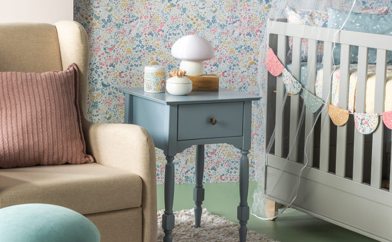 decoração de quarto infantil contendo: parede colorida; poltrona rosa com almofada rosa; puffe azul; criado mudo azul com luminária em cima; berço azul claro com véu.