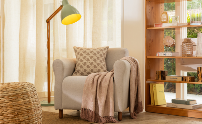 cantinho da leitura com poltrona, almofada, manta, estante com diversos itens decorativos e luminária de chão
