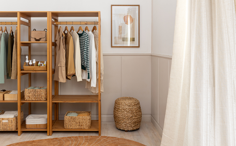 quarto organizado com arara de roupas de madeira, com cabides, diversas peças de roupas organizadas, puff, quadro decorativo e caixas organizadoras para ajudar na divisão dos objetos.