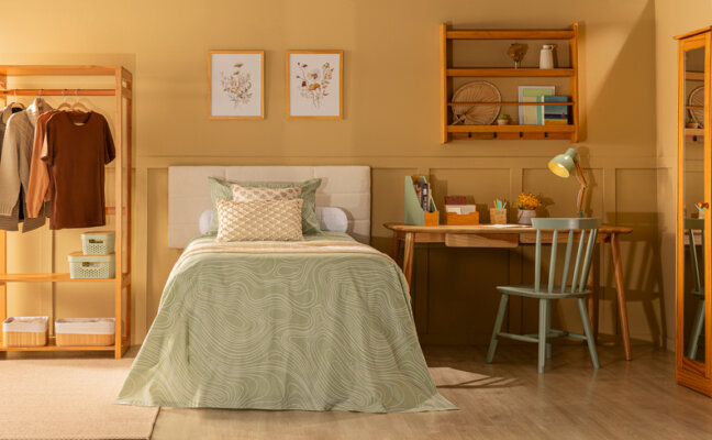 roupa de cama solteiro com tons pastel em um quarto com arara de roupas, mesa e cadeira