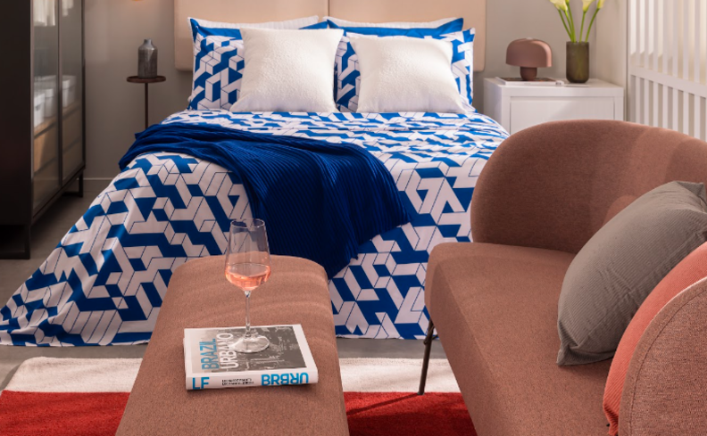 quarto decorado no estilo contemporâneo, com cama, roupa de cama zul, sofá, almofadas, mesa de centro e guarda-roupa