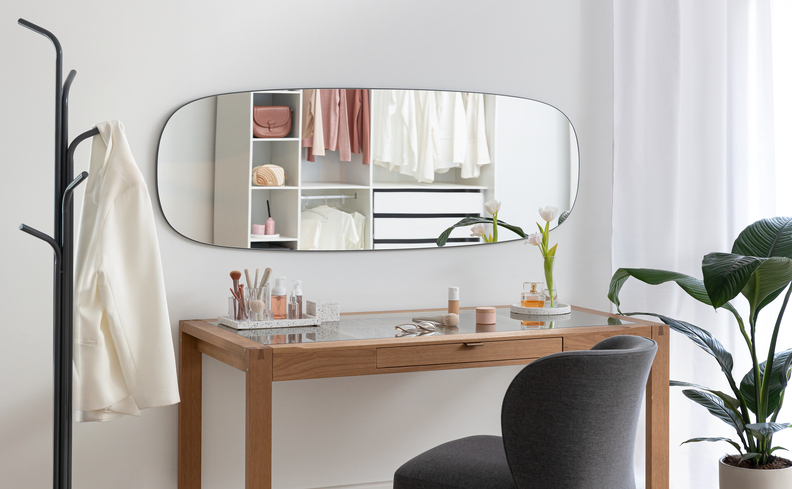 espelho orgânico na horizontal em uma penteadeira com cadeira, cabideiro e vaso de planta decorativo