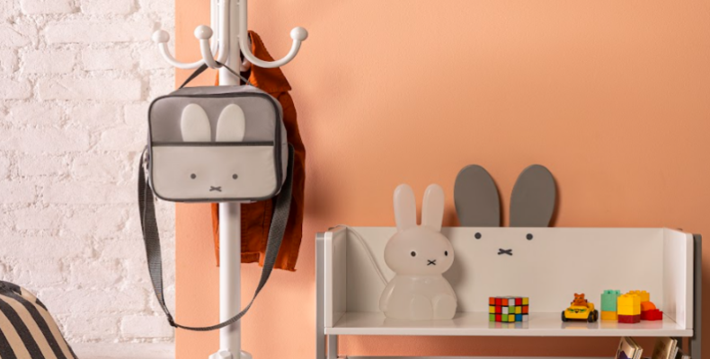 ambiente com lancheira térmica pendurada em um cabideiro, uma mesa com luminária de coelho e outros itens decorativos