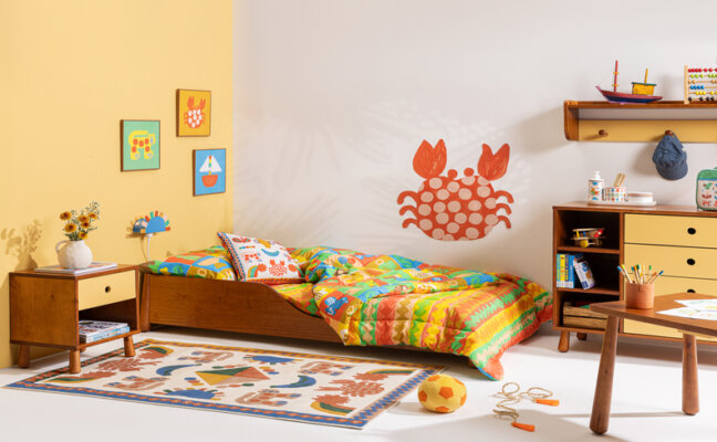 quarto infantil decorado com a linha caxixi com cama, tapete, edredom, cômoda, mesa de cabeceira e outros itens decorativos