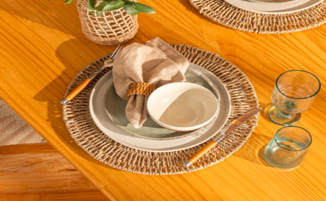 guardanapo de tecido na mesa posta com prato raso e fundo, jogo americano, taça. talheres e vaso de planta