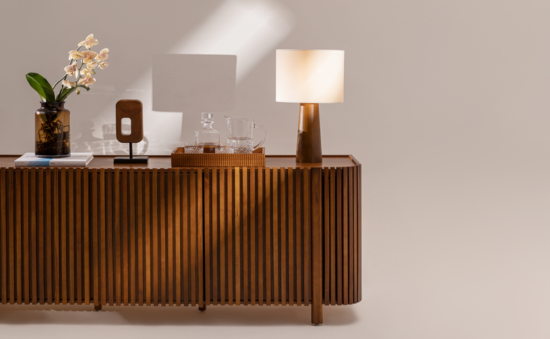 buffet pequeno para sala de jantar de madeira ripada, itens decorativos como abajur, bandeja com copo e garrafa, além de adorno de mesa