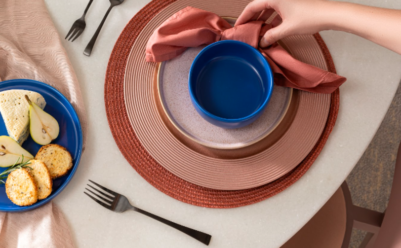 mesa posta para petiscos com sousplat, jogo americano, prato fundo e prato de sopa, além de guardanapo de tecidos e talheres