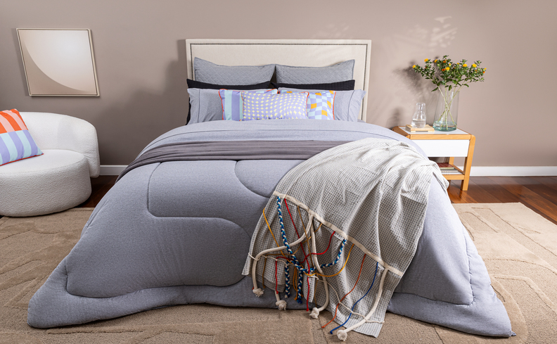 decoração de quarto com cama de casal com roupa de cama completa, peseira, poltrona e mesa de cabeceira