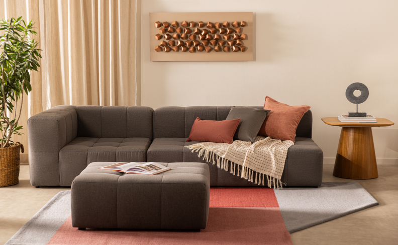 sofá cinza retrátil em uma sala de estar cinza e branco, com detalhes decorativos coloridos