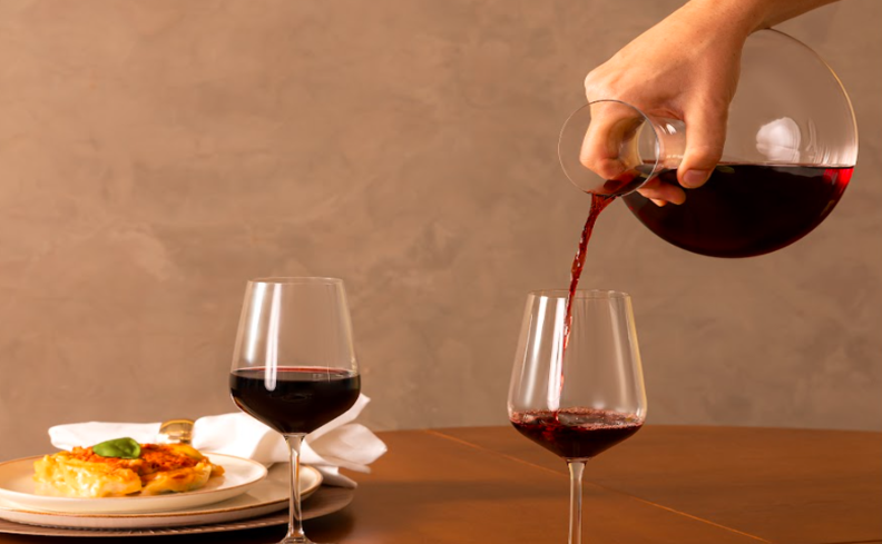 tipos de vinho para servir em diversas ocasiões, com duas taças de vinho tinto e uma pessoa servindo a bebida em um decanter de vinho
