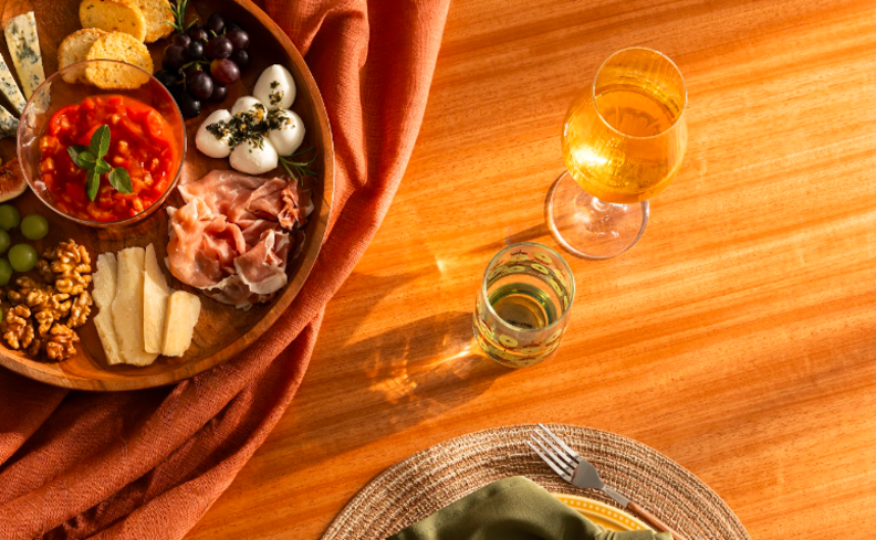 vinho verde para escolher entre os tipos de vinho para diversas ocasiões em uma mesa posta com taça de vinho, tábua de frios e outros itens