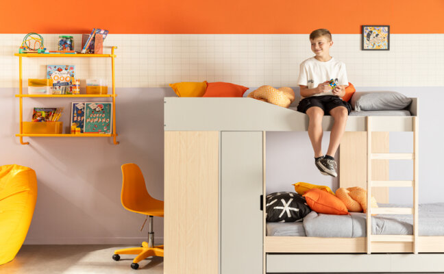 menino sentado em uma beliche em um quarto decorado com tema de esporte para crianças para inspirar a prática de esportes