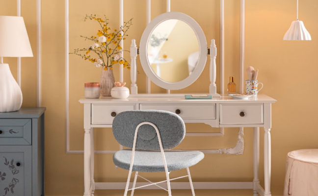 estilo romântico na decoração do quarto com uma penteadeira com espelho, vaso com flores, cadeira em tom de azul e tons claros na parede.