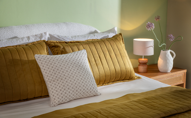 quarto aconchegante casal com travesseiros, almofadas e uma iluminação indireta com abajur para ter um quarto aconchegante e funcional