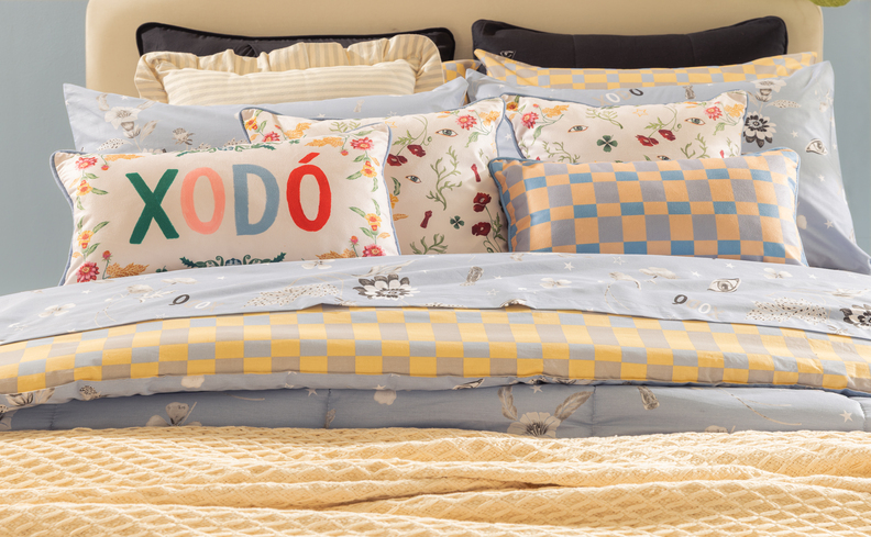 quarto com decoração romântica cama posta com edredons em tons de azul e amarelo pastel, além de diversas almofadas e travesseiros.
