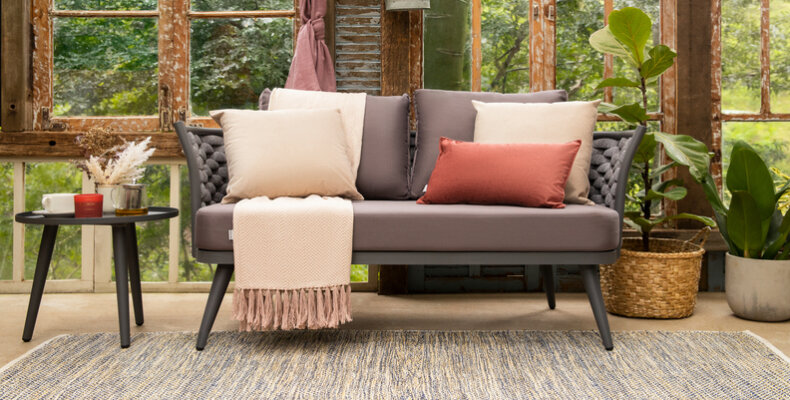 decoração para jardim de inverno com sofá, almofadas, manta, plantas em casos, mesa lateral e itens decorativos