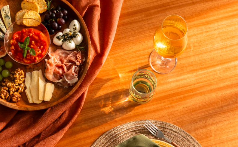 taça de vinho branco em uma mesa, com uma tábua de petiscos, sousplat e pratos.