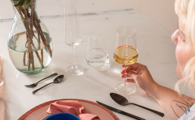 dicas de como servir vinho em um ambiente de mesa posta com uma mulher segurando uma taça de vinho rose.