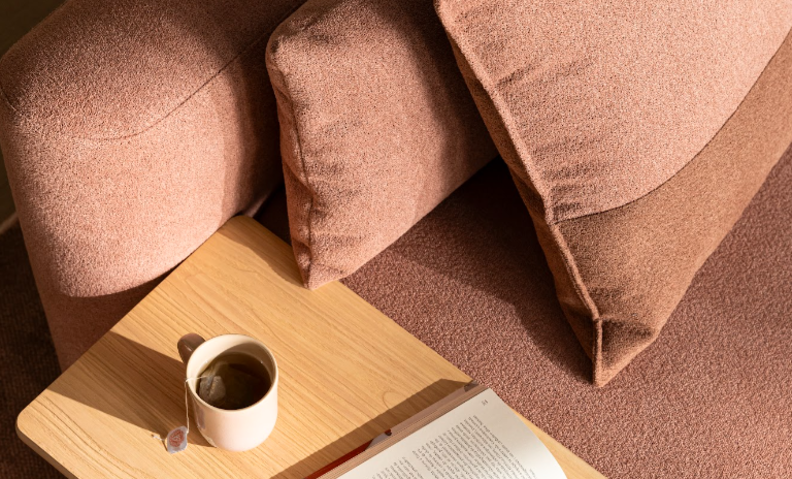 decoração aconchegante de inverno na sala de estar com sofá em tons de marrom, mesa lateral de madeira com uma xícara de chá e um livro.