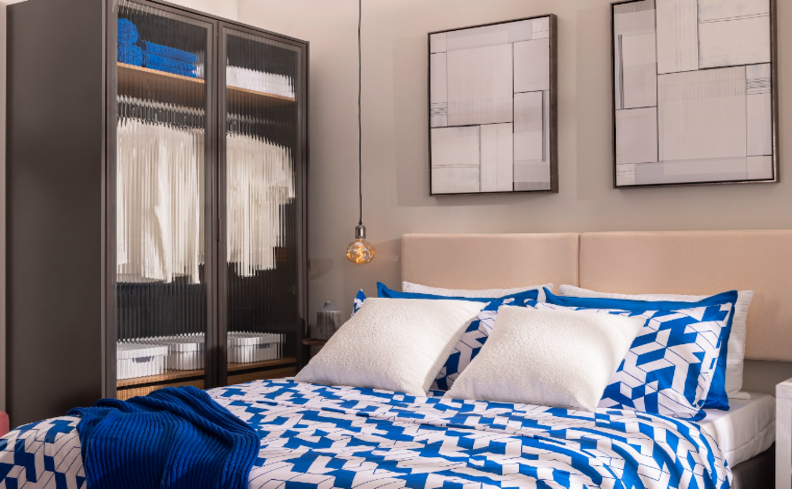 guarda-roupa de canto de casal em um quarto, além de cama com roupa de cama azul, quadros decorativos e travesseiros.