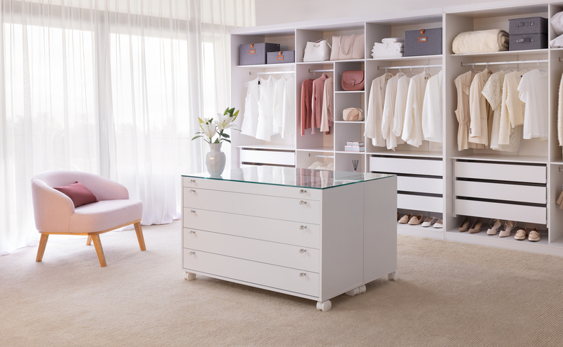 tamanho padrão de guarda-roupa de casal em um ambiente amplo de closet com poltrona e cômoda no meio do cômodo.