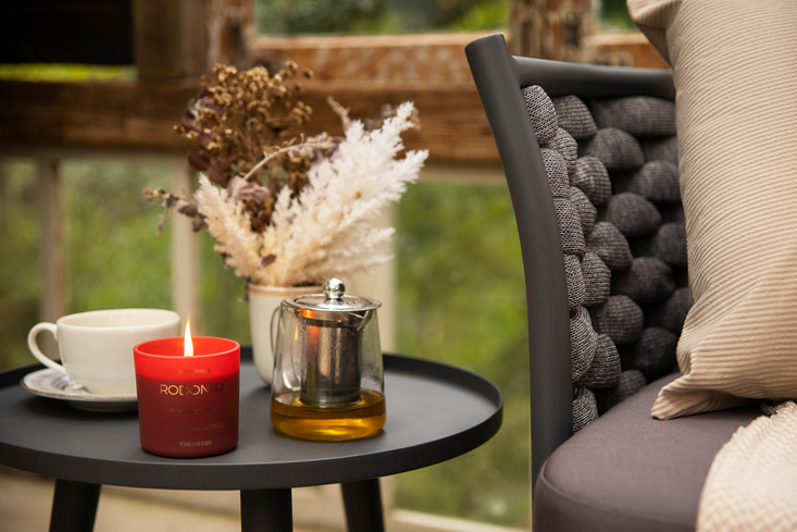 mesa lateral com uma vela decorativa, vaso com flores e um bule de chá em um ambiente externo com uma decoração de inverno