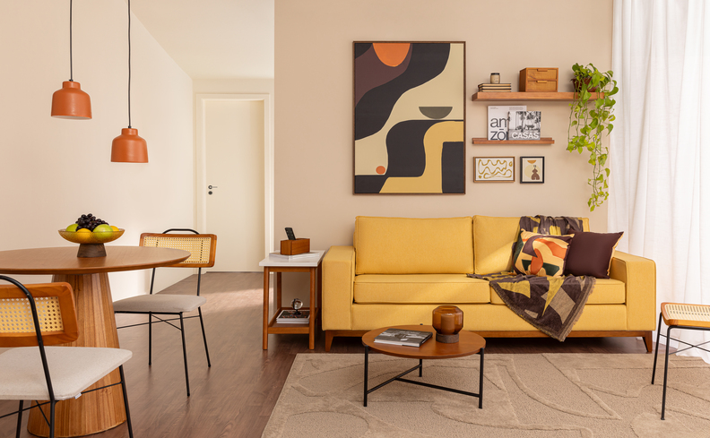 sofá cama para apartamento pequeno amarelo na sala de estar, além de mesa de centro, mesa de jantar, cadeiras, lustres pendentes, prateleiras e quadros decorativos.