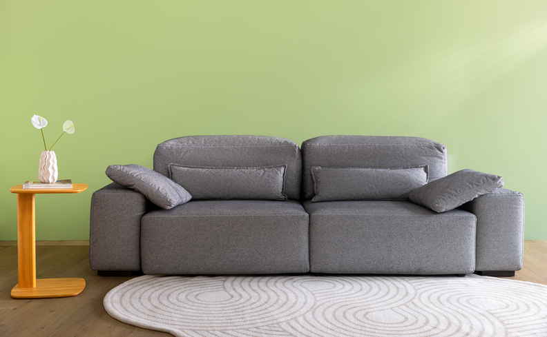 sofá para sala pequena de apartamento, tapete e mesa lateral com um vaso com flores.