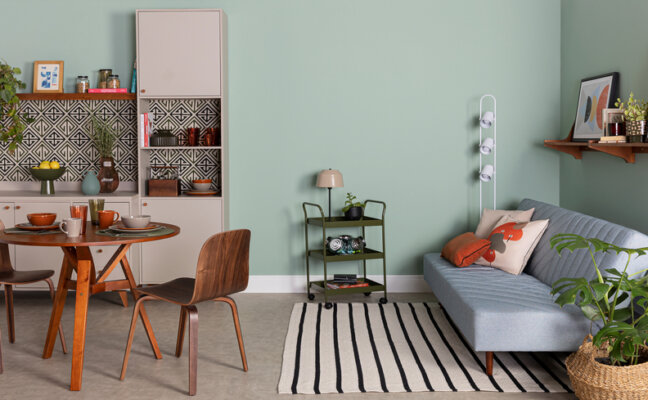 sofá para apartamento pequeno na sala de estar integrada com cozinha, além de tapete, mesa de jantar, cadeiras, armários e itens decorativos.