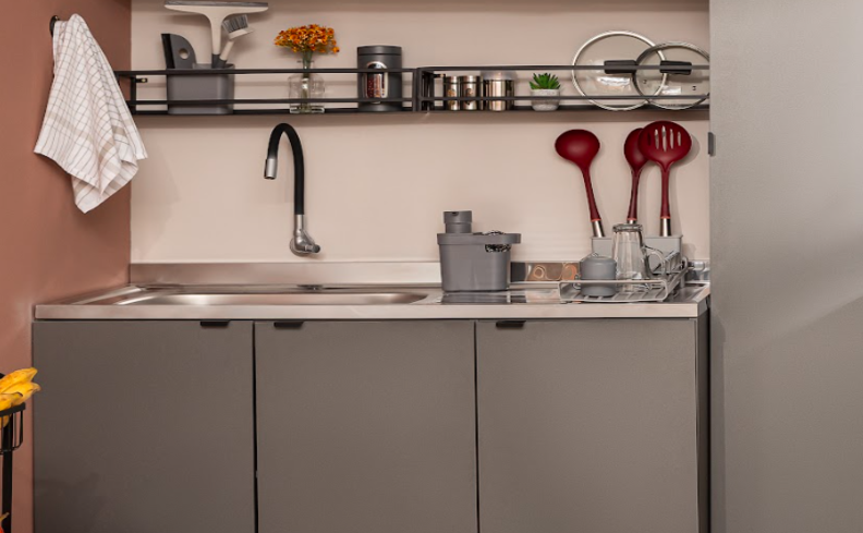 itens de cozinha em uma bancada com pia, armários, utensílios, estantes e diversos itens que ajudam no preparo.